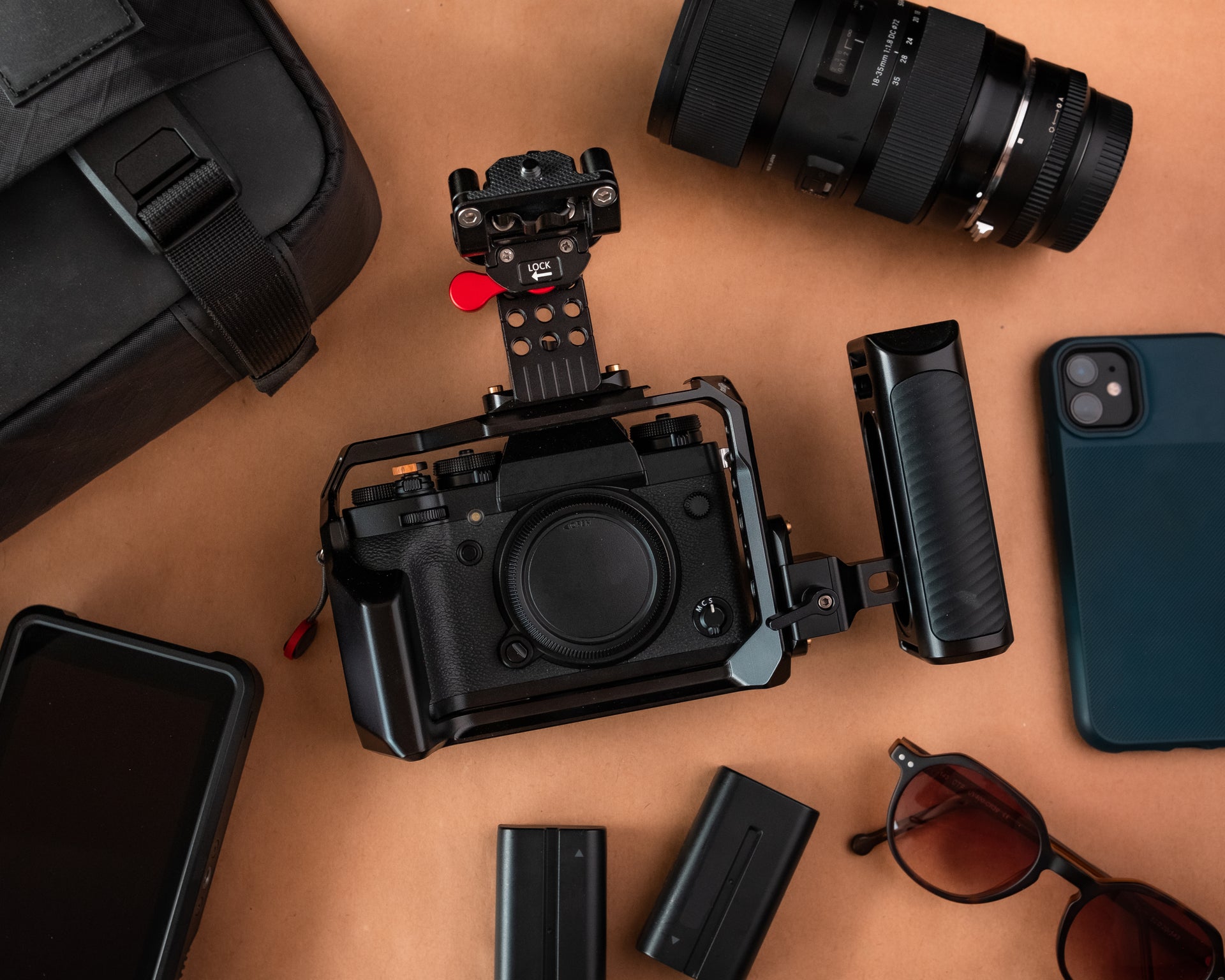 <img src="camera-rig-accessories-brown-background.jpg" alt="Professional camera in cage with two batteries, iPhone, external monitor, travel case, glasses and camera lens on brown background">